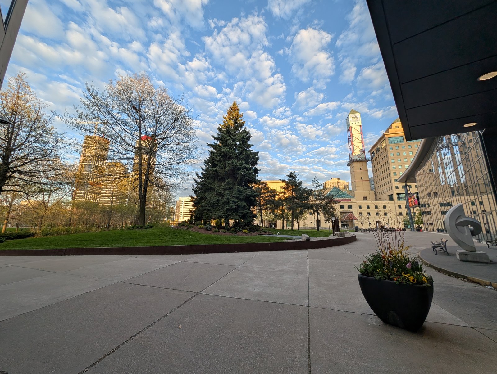 Glass exterior of the Living Arts Centre beside trees and downtown Mississauga buildings.