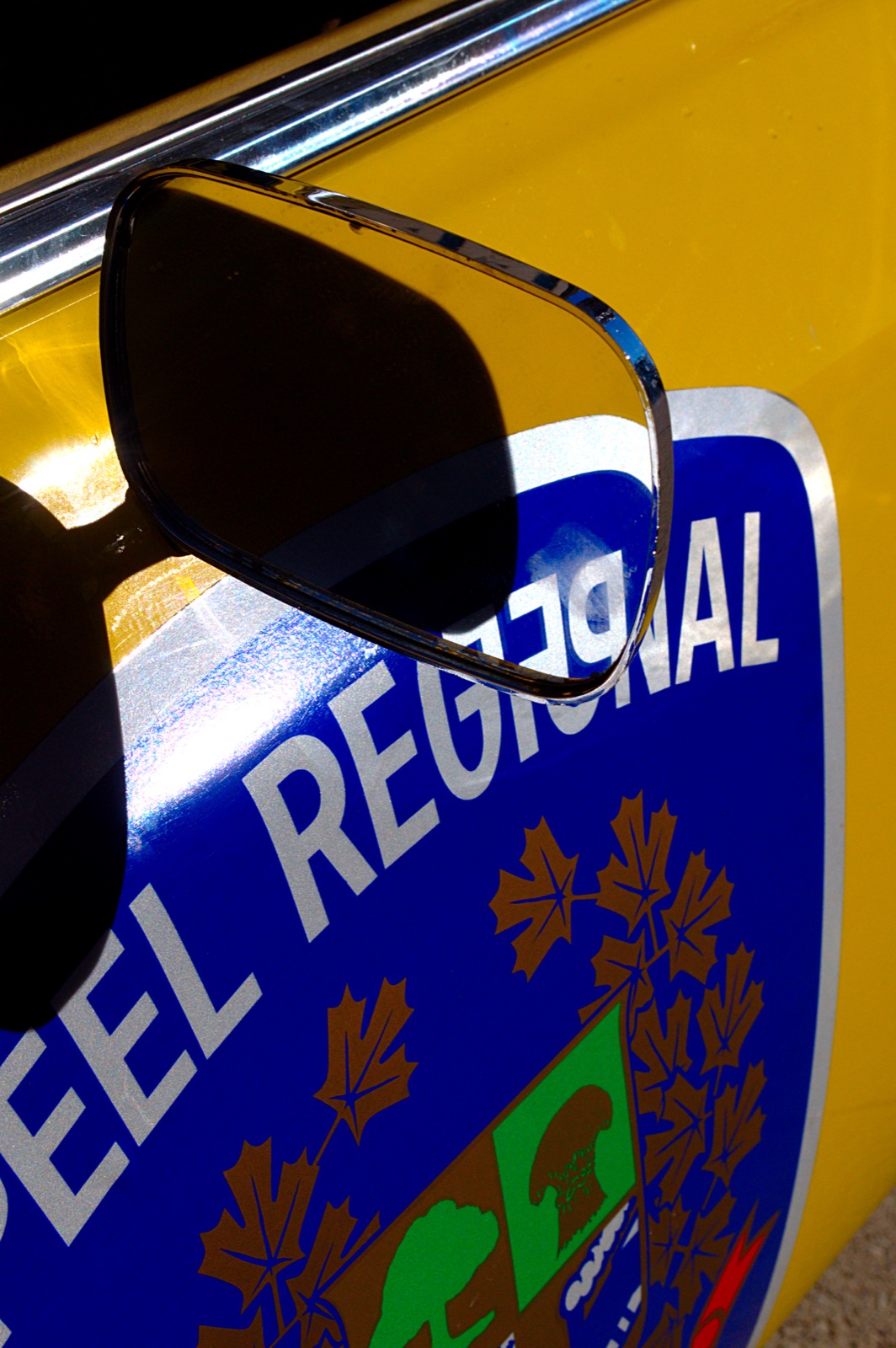 Close-up of Peel Regional Police insignia and the mirror on a historic yellow cruiser.